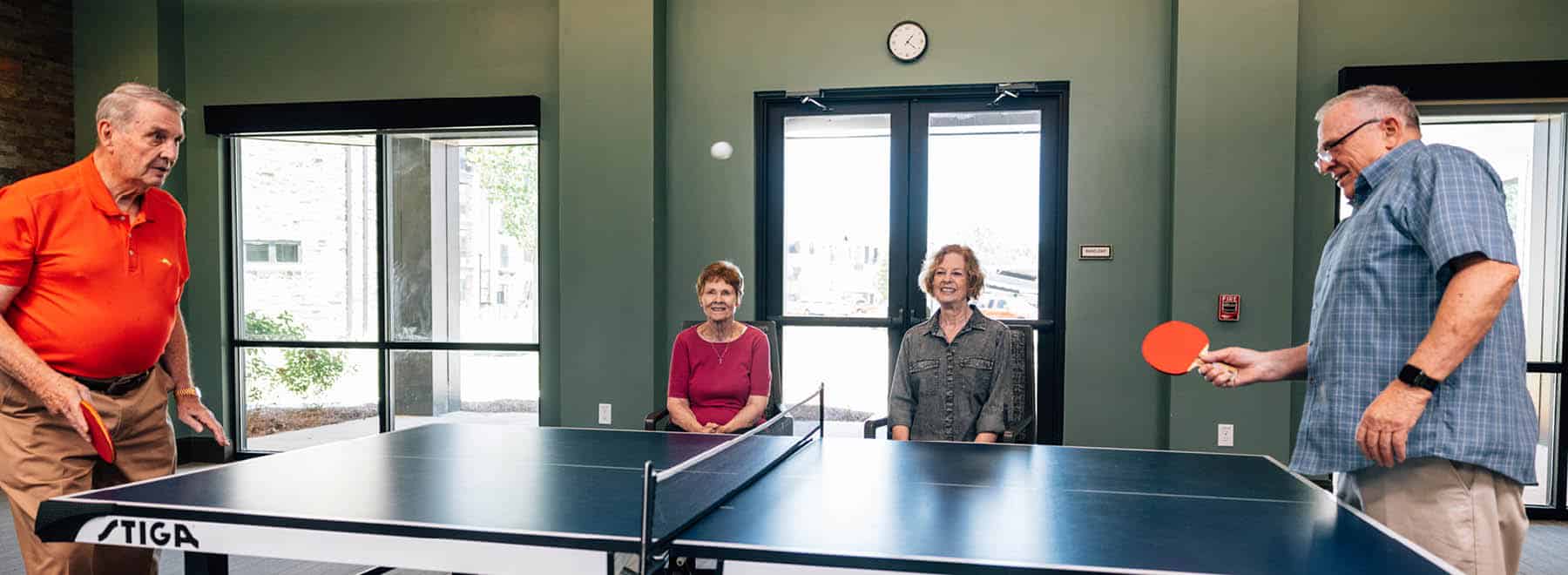Two resident couples -- two ladies seated watching their husbands play ping pong